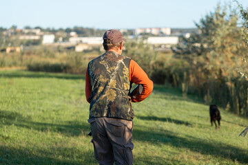 Mature hunter man holding a shotgun and walking through a field