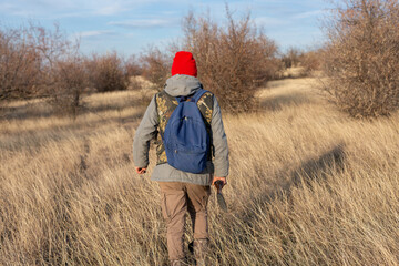Mature hunter man holding a shotgun and walking through a field