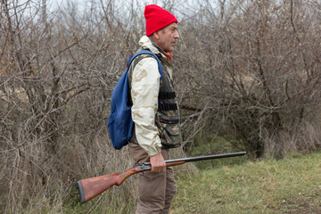 Mature hunter man holding a shotgun and walking through a field