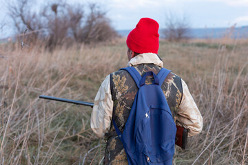 Mature hunter man holding a shotgun and walking through a field