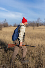 Mature hunter man holding a shotgun and walking through a field