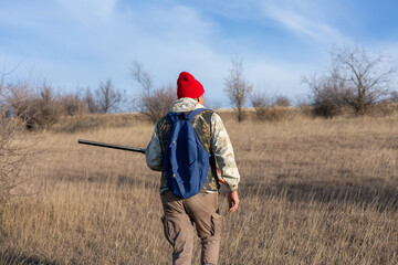 Mature hunter man holding a shotgun and walking through a field