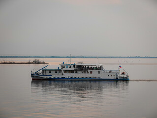 A riverboat sails gently across calm waters during sunset, highlighting a serene atmosphere. the boat makes its way with stillness, surrounded by a vast expanse of water and a distant shoreline. the