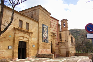 Fototapeta premium Old brick church with an open wooden door, a small bell tower, and a religious banner on the facade; leafless trees and a traffic sign nearby;