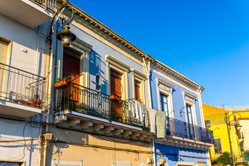 A scenic view of colorful italian vintage buildings with vibrant facades, featuring green shutters and quaint balconies, under a soft, warm light creating a picturesque ambiance