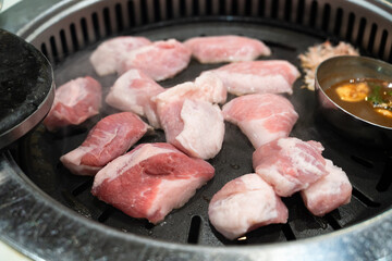 Grilling pork meat on a iron BBQ board in Korean restaurant.