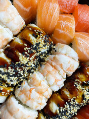 Five kinds of rolls with rice, tuna, salmon and shrimp sprinkled with white and black sesame seeds neatly folded together, close-up, top view. Japanese cuisine.