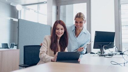 Talented businesswomen collaborate on a tablet in a modern office, driving teamwork and innovation