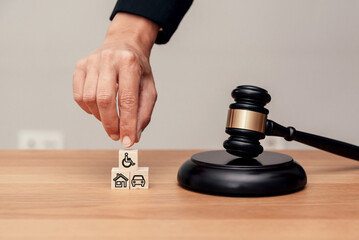 Close up of Hand stacking blocks with disability, house and car icons near judge gavel