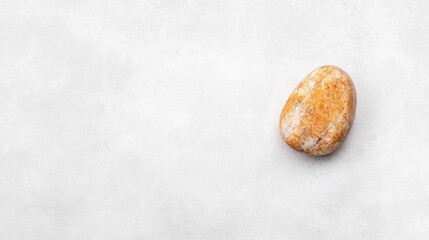 A single, smooth, light brown rock with a rough, uneven surface sits on a white background.