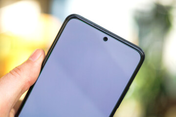 A close-up of a modern smartphone with a blank screen, held in a person's hand. The background is...