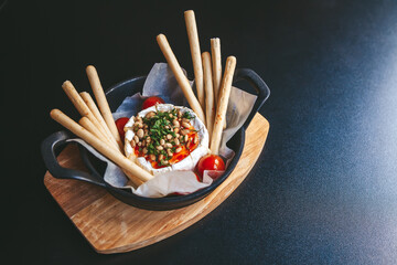 Baked camembert cheese with herbs and pine nuts, served in a cast iron skillet with breadsticks and...