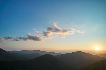 Sun sets behind rolling hills, casting warm, golden glow across sky. Wispy clouds, tinged with hues...