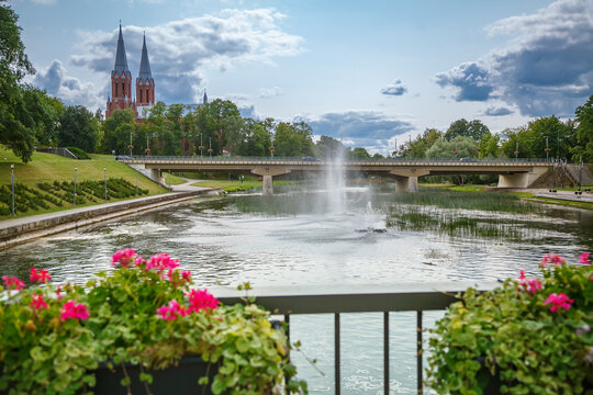 Picturesque park in Anyksciai, Lithuania, featuring a fountain spraying water, and a church with twin spires in the background