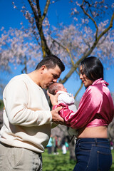 Fototapeta premium Loving parents kissing newborn baby in blooming park