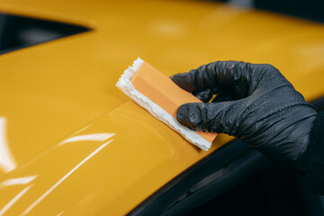 Car detailing worker applying ceramic car coating on yellow car at workshop