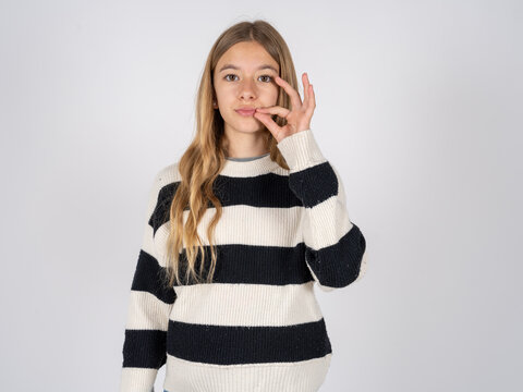 beautiful caucasian teen girl wearing striped sweater mouth and lips shut as zip with fingers. Secret and silent, taboo talking.