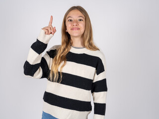 beautiful caucasian girl wearing striped sweater pointing finger up and looking inspired by genius thought, showing good idea sign, having clever solution in mind