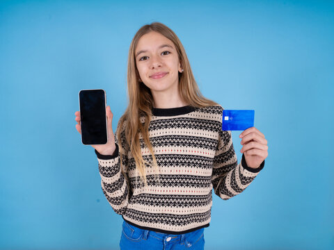 beautiful caucasian girl wearing striped sweater opened bank account, holding smartphone and credit card, smiling, recommend use online shopping application
