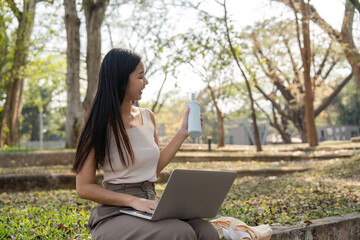 Sustainable lifestyle. Young woman multitasking with her laptop and reusable cup.
