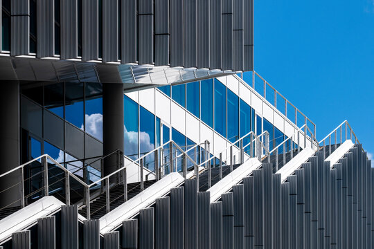 Futuristic staircase with angular metallic design against a blue sky. Modern architectural detail emphasizing structural aesthetics and contemporary urban development.