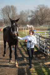 Young horsewoman leading her horse in a riding stable paddock