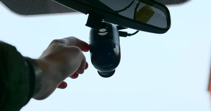 Driver pressing the power button on a dash cam mounted on the windshield, ensuring safety and security while traveling on the road
