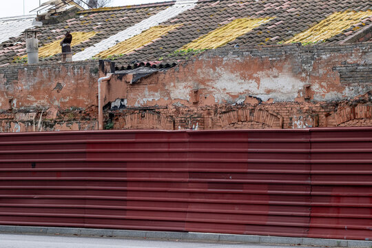 Weathered brick wall with faded yellow markings and red metal fence. Urban decay meets industrial textures in a visually striking city composition.