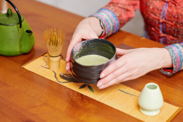 Woman arranging matcha whisk and green teacup on wooden tray during traditional tea preparation process, showcasing harmony and elegance