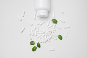 White capsules, pills, tablets spilled out of white jar on light background. Minimalistic concept...