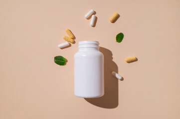 Minimalistic concept of vitamins, dietary supplements, nutraceuticals. Capsules, pills, tablets, white jar, green leaves on beige background. Medical pharmacological background
