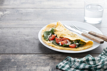 Stuffed omelette with tomatoes and spinach on wooden table. Copy space