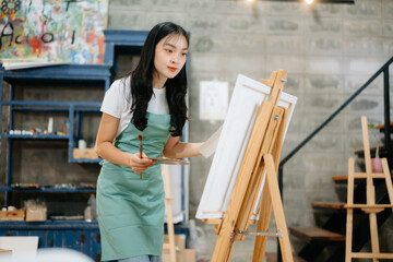 Cheerful female artist painting in a vibrant studio with brushes, a palette, and a blank canvas.