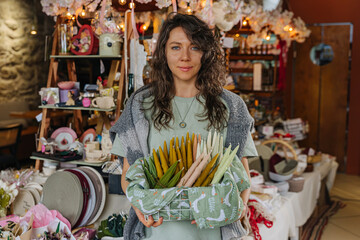 Artisan organizing handcrafted decor at a market stall.  Colorful handmade candles, flowers, and decor at craft fair.