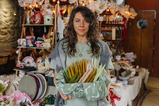Artisan organizing handcrafted decor at a market stall.  Colorful handmade candles, flowers, and decor at craft fair.