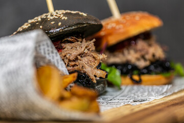 Burger with pulled meat in a dark and light bun with fresh vegetables and french fries on a wooden board. Fast food. Close up