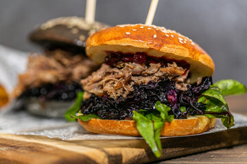 Burger with pulled meat in a dark and light bun with fresh vegetables and french fries on a wooden board. Fast food. Close up