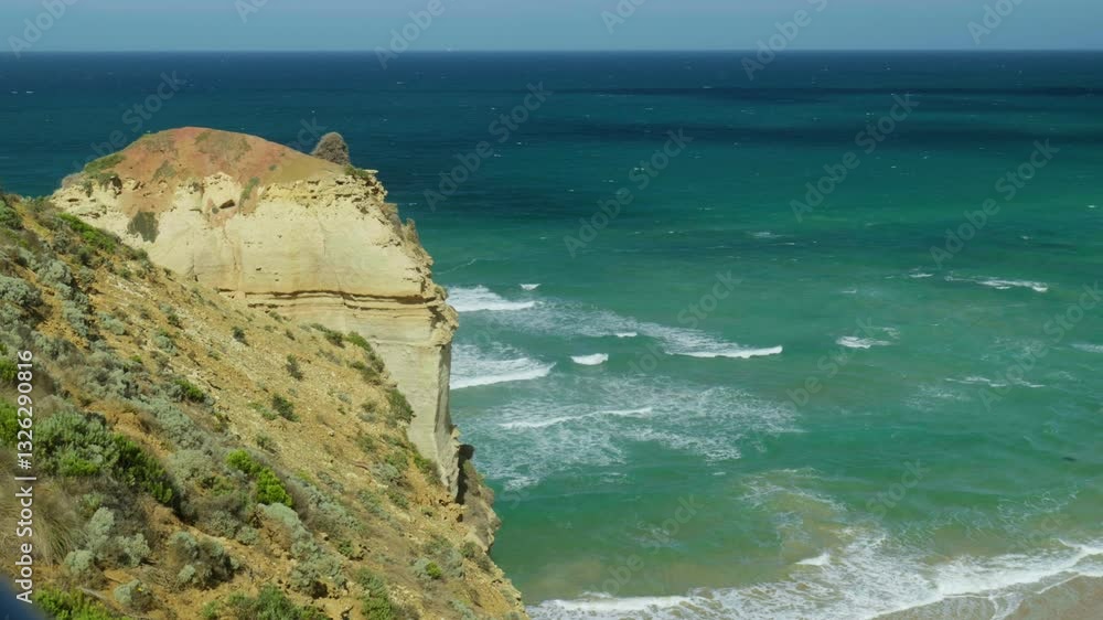 Poster waves breaking powerfully against rocks below a rugged cliff edge, showcasing the dynamic interactio