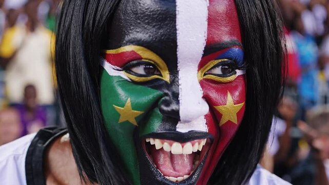 Joyful South Sudanese sports fan with vibrant flag face paint cheering in a stadium  

