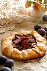 Plum galette on a parchment paper, close-up view. Delicious rustic tart