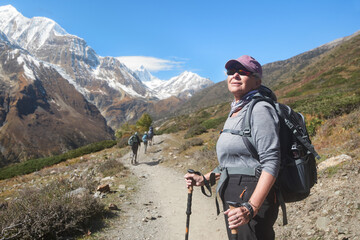 Happy elderly woman hiker with backpack follows her group high in mountains during trek around Annapurna, Nepal.