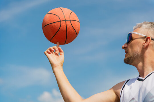 Man spins basketball on his finger against a clear sky during outdoor practice session