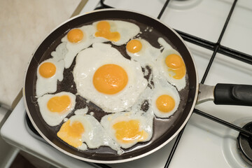 Chicken egg and 9 quail eggs in frying pan.