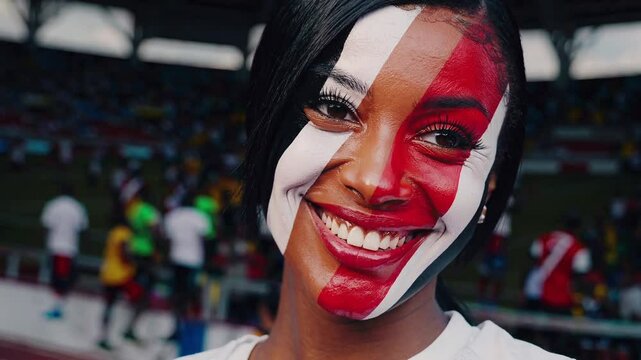 Smiling Trinidadian and Tobagonian sports fan with bold flag face paint at a stadium  
