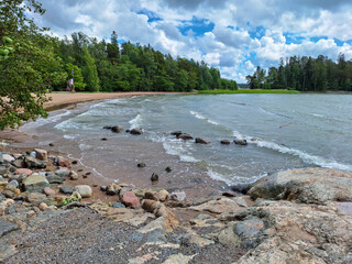 Saaronniemi Beach in Ruissalo, Turku, Finland during a sunny summer day with clouds rolling in and the waves splashing and hitting the rocky shore