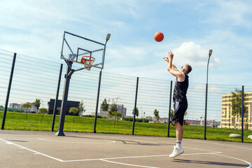 Basketball player makes a leap to shoot a basket on an outdoor court during a sunny day