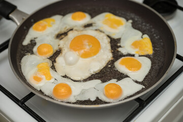 Chicken egg and 9 quail eggs in frying pan.