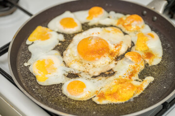 Chicken egg and 9 quail eggs in frying pan.