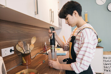 Girl using hand blender preparing sauce in domestic kitchen