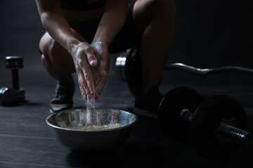 Woman applying talcum powder onto her hands above bowl before training in gym, closeup